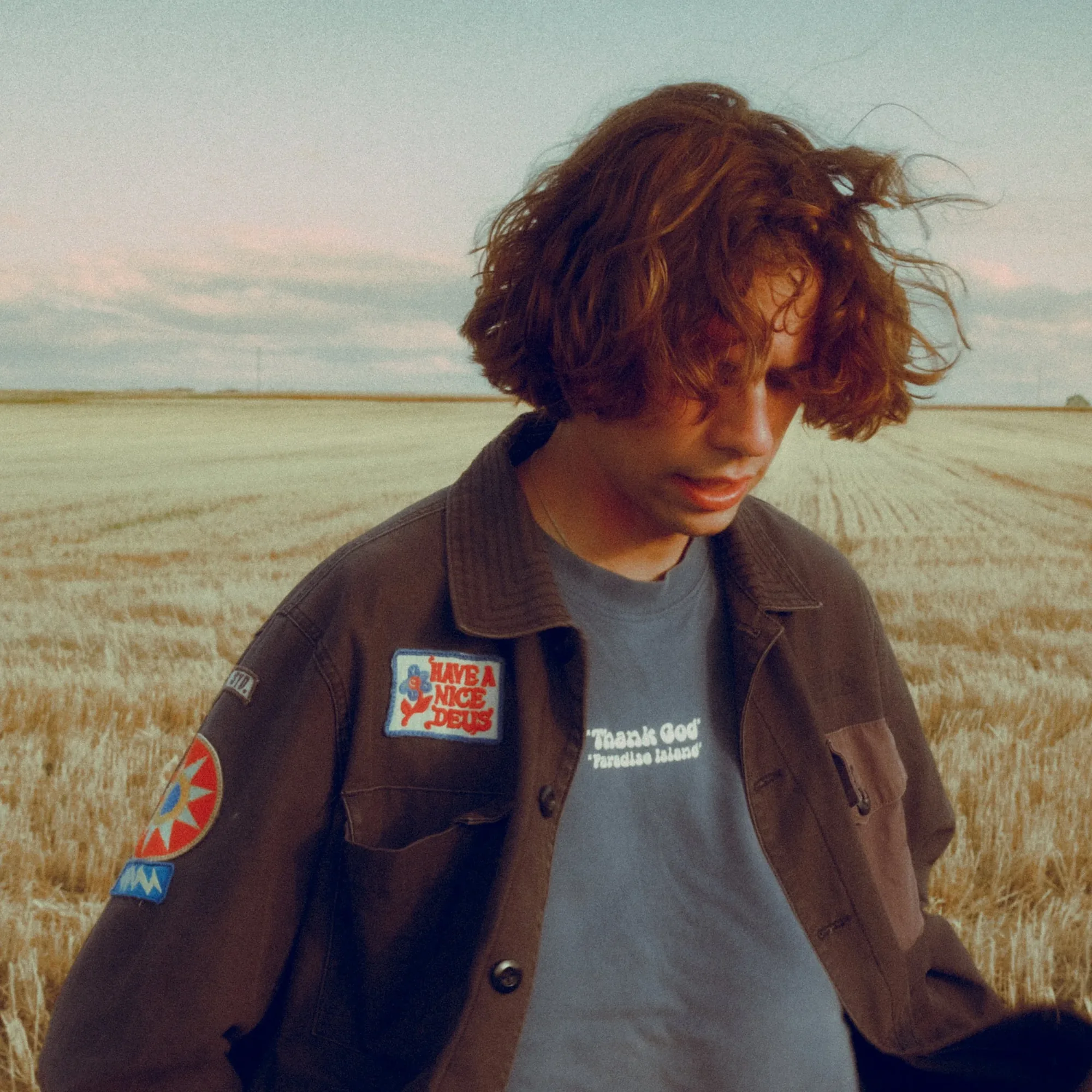 Pijus in a wheat field, wearing a patched brown jacket